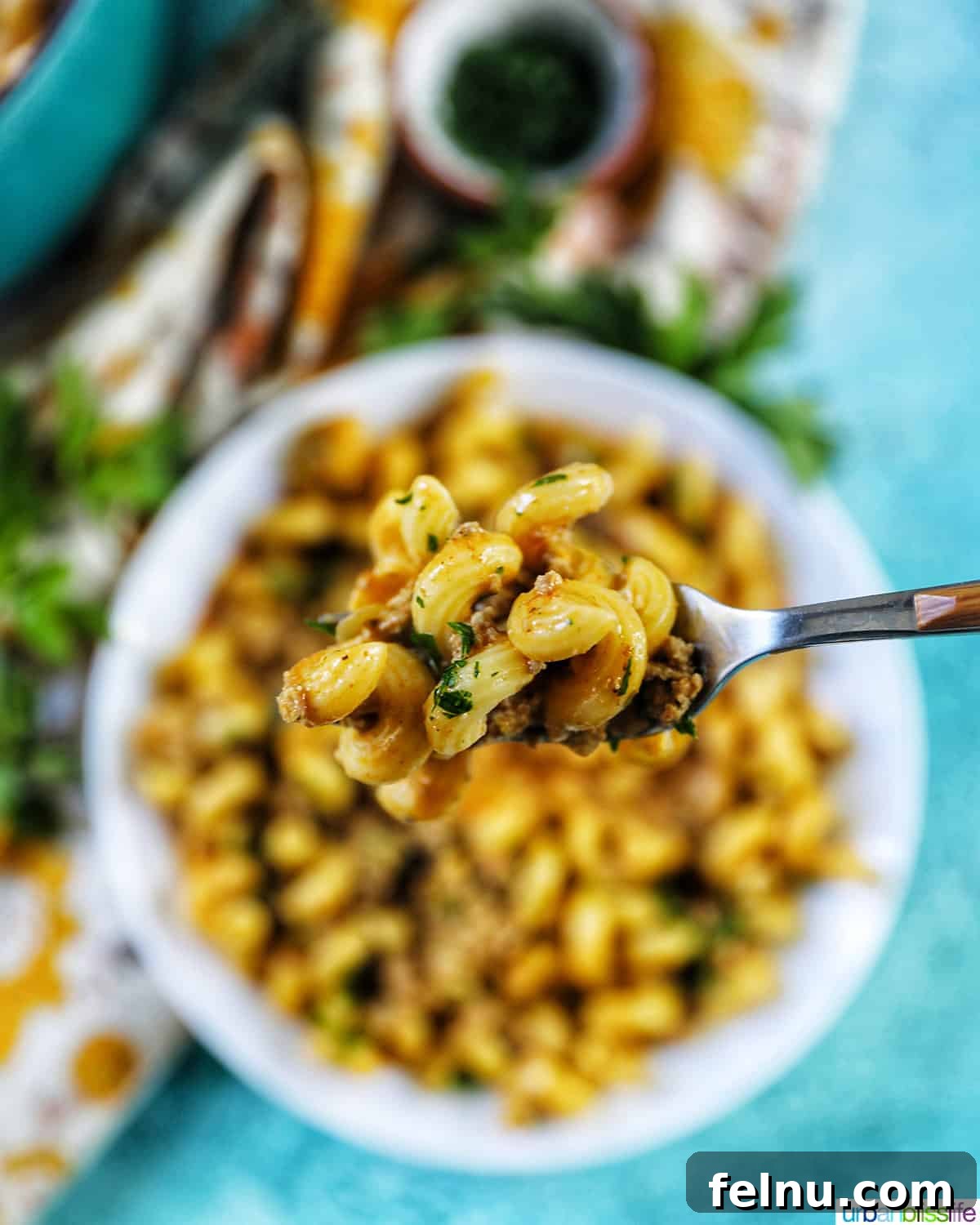 Creamy Dairy-Free Cheeseburger Mac Skillet 3 A forkful of creamy dairy-free cheeseburger pasta held above a serving bowl, showcasing the rich texture and deliciousness.