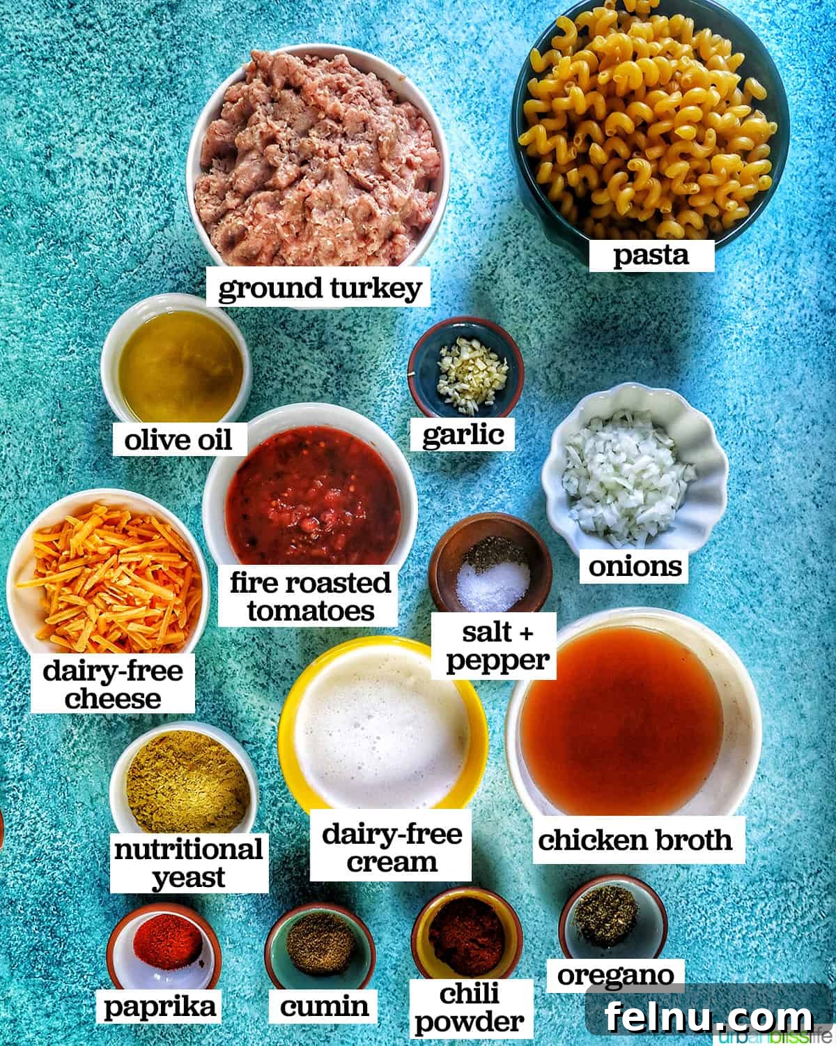 Creamy Dairy-Free Cheeseburger Mac Skillet 4 A vibrant collection of ingredients for one-pot dairy-free cheeseburger pasta, neatly arranged in bowls on a bright blue background.