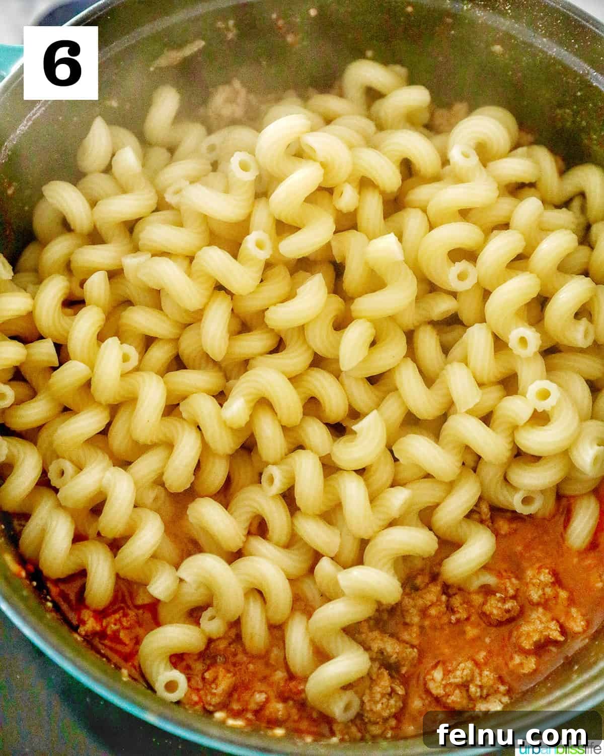 Creamy Dairy-Free Cheeseburger Mac Skillet 10 Uncooked pasta being added directly into the flavorful sauce mixture in the Dutch oven, ready to cook together.