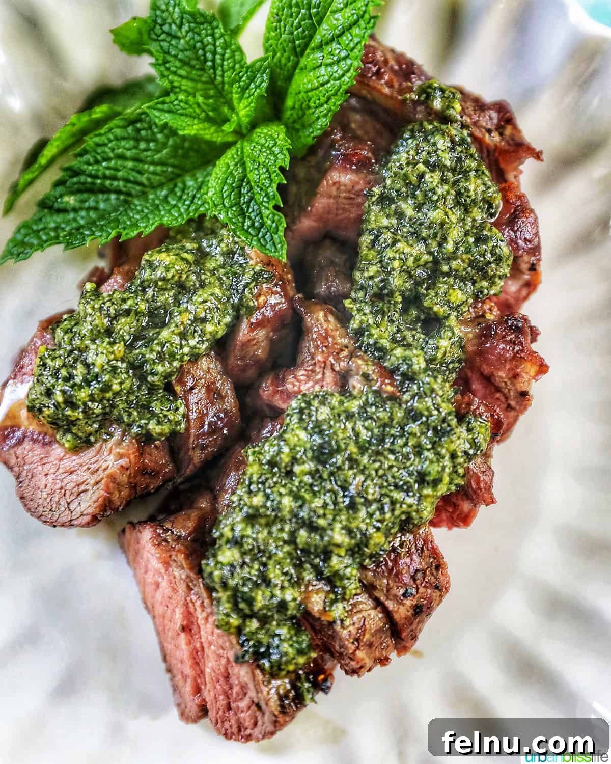 Zingy Mint Pesto 12 Succulent steak slices generously topped with fresh mint pesto, artfully garnished with mint leaves on a pristine white scalloped plate.