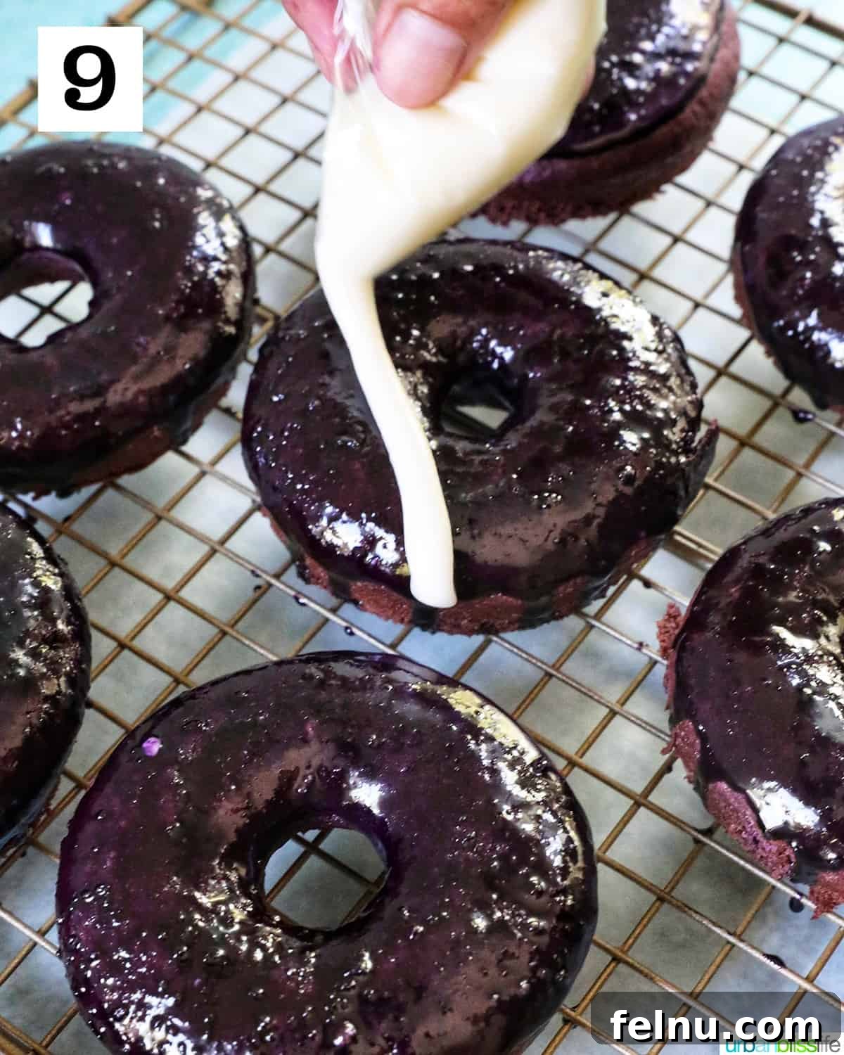 Ube Dream Donuts 17 Several ube donuts on a baking rack with a hand drizzling white glaze over donuts.