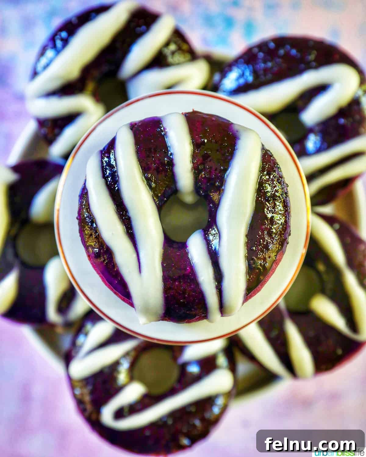 Ube Dream Donuts 20 Several ube donuts with ube glaze and white glaze drizzle, one on a pedestal in the middle.