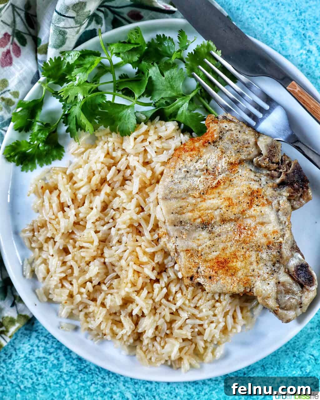 Instant Pot Pork Chop Rice Bowl 2 Instant Pot Pork Chops and Rice served on a white plate with a side of greens, fork, and knife.