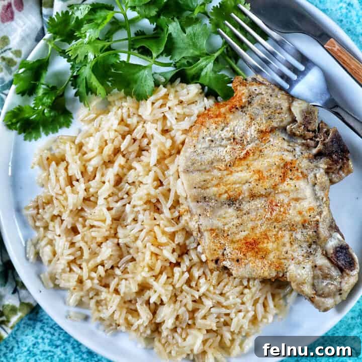 Instant Pot Pork Chops and Rice on a white plate with side of greens and fork and knife.