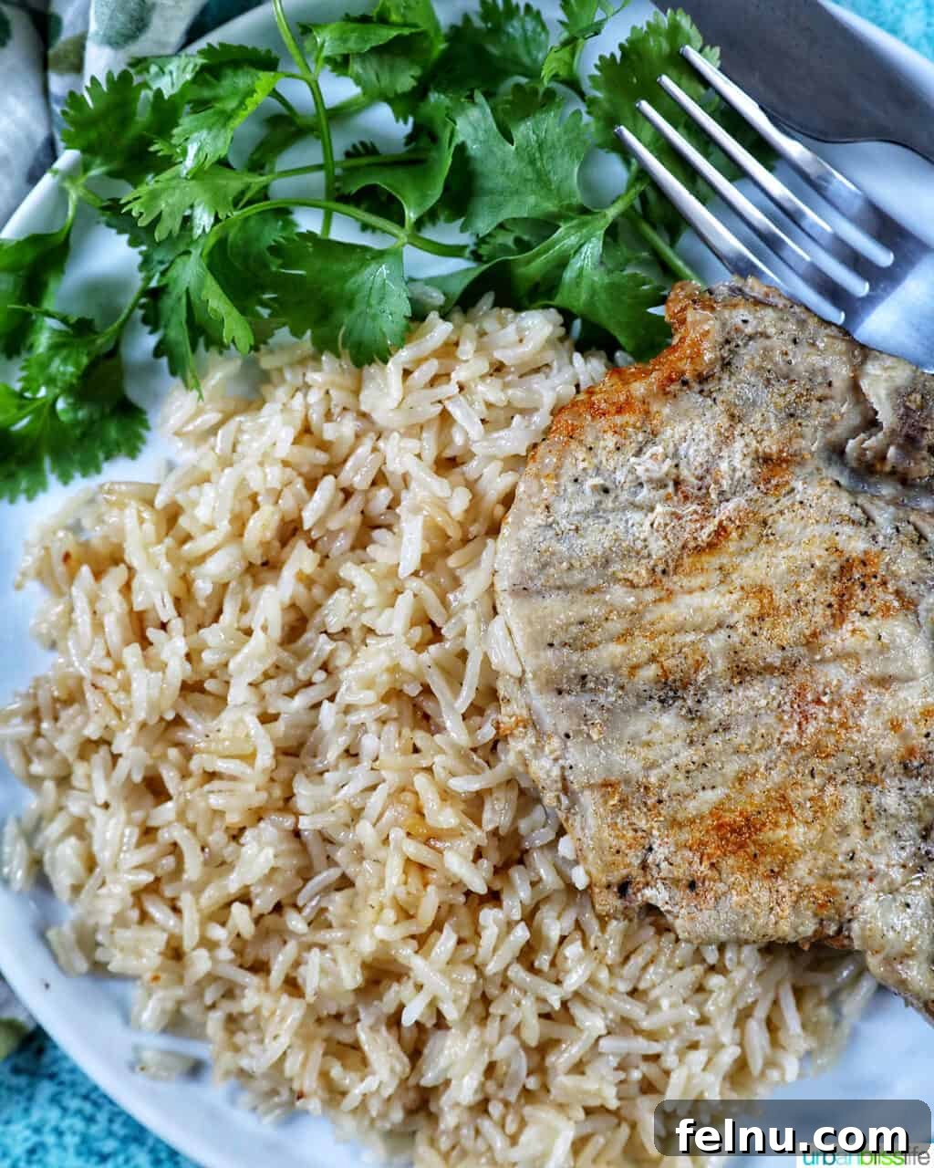 Instant Pot Pork Chop Rice Bowl 3 Close-up shot of Instant Pot Pork Chops and Rice on a white plate, accompanied by a side of greens, fork, and knife.