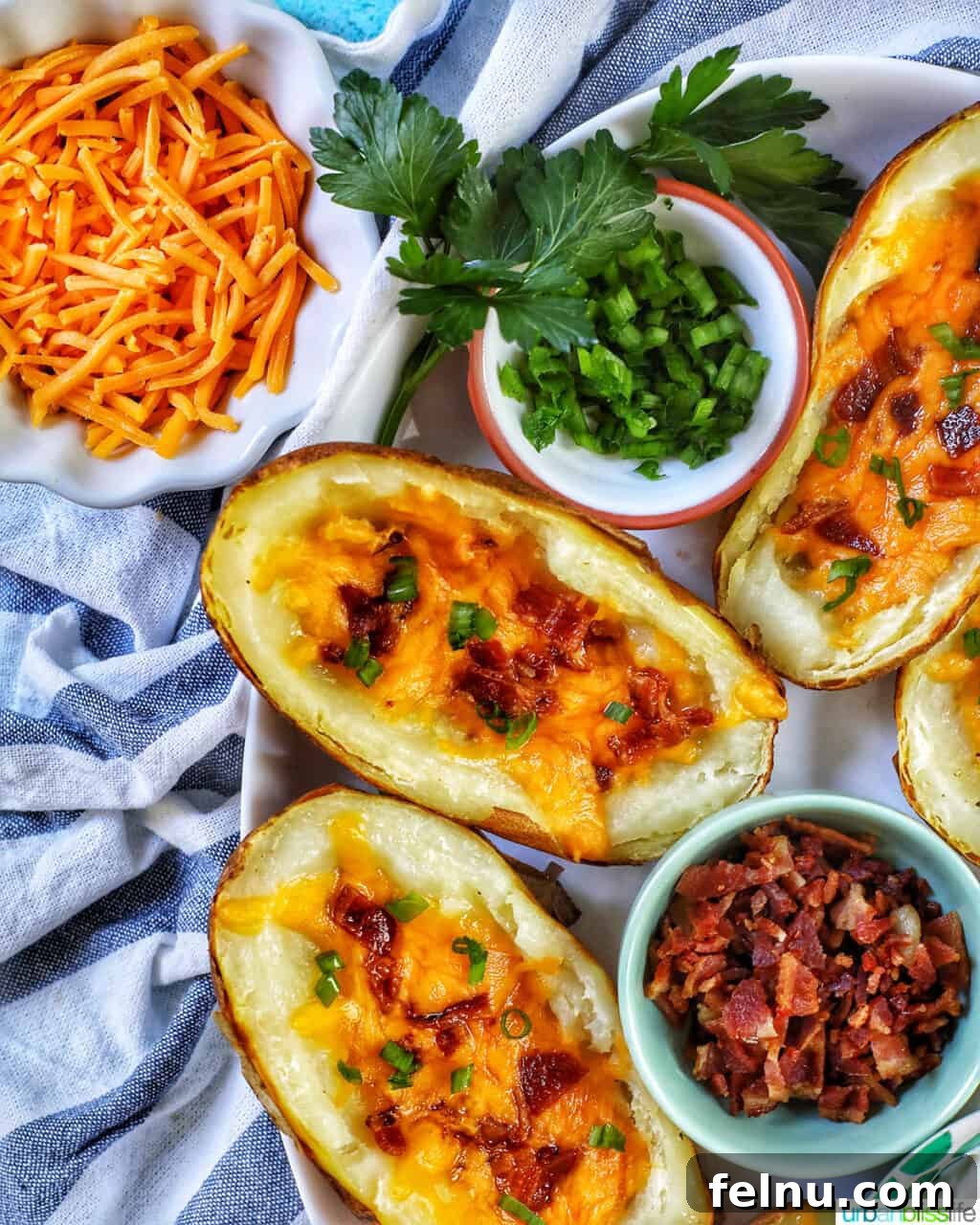 Ultimate Air Fryer Potato Skins 16 air fryer potato skins with sides of shredded cheddar cheese, green onions, bacon, on a white and blue napkin.