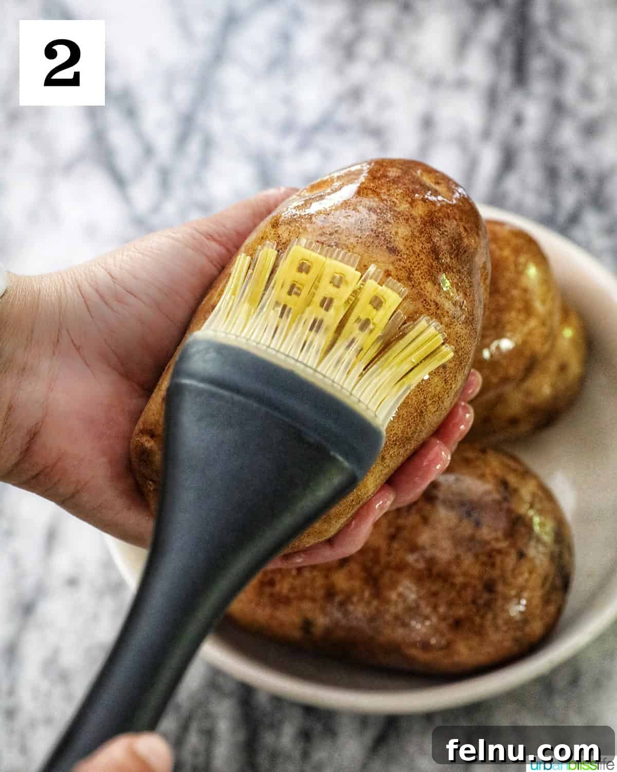 Ultimate Air Fryer Potato Skins 6 a hand holding a potato while the other hand brushes olive oil over the potato skin.