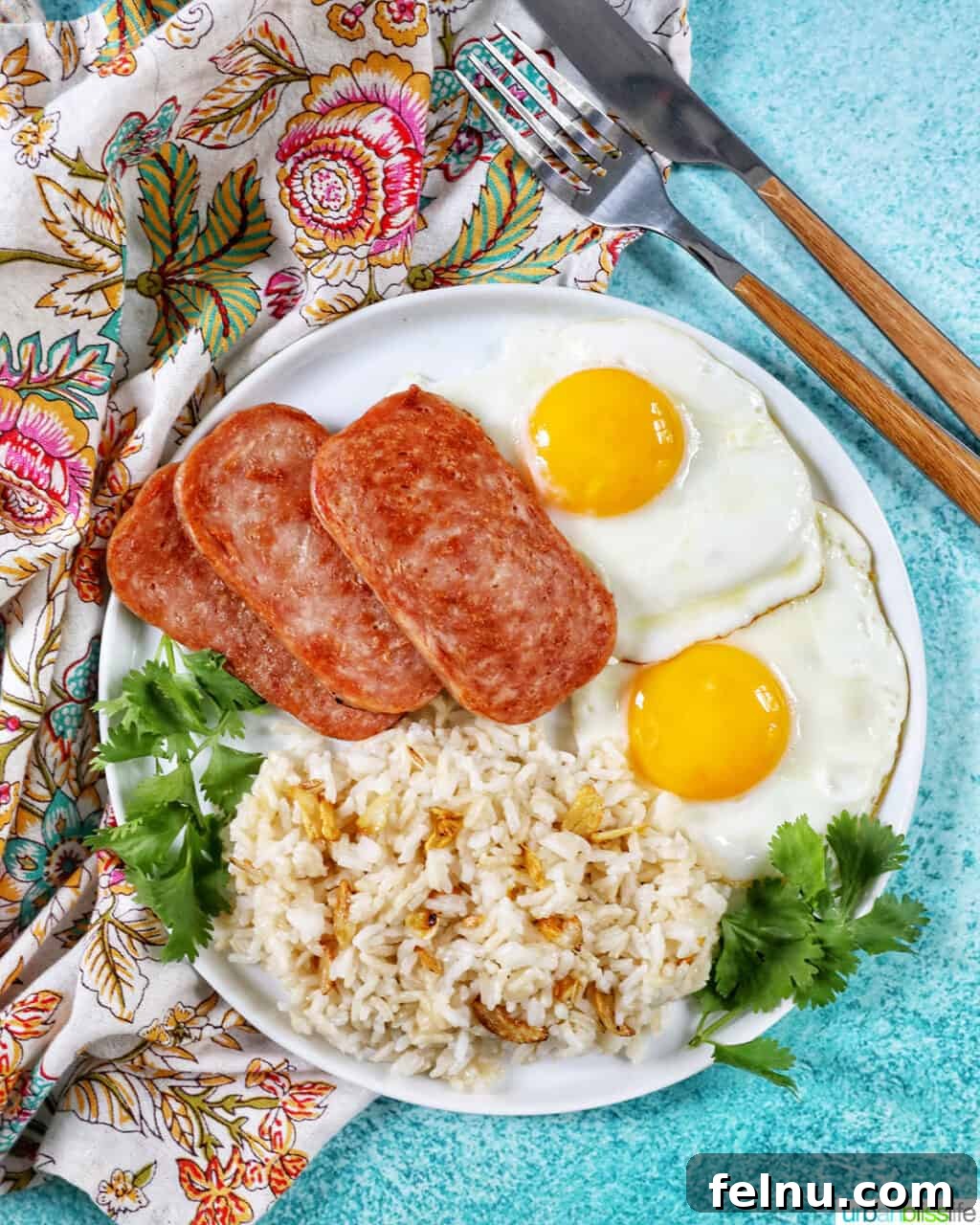 Spamsilog A Filipino Breakfast Classic 3 Plate of Spamsilog: slices of Spam, two eggs over easy, and Filipino Sinangag garlic rice with greens and fork and knife.