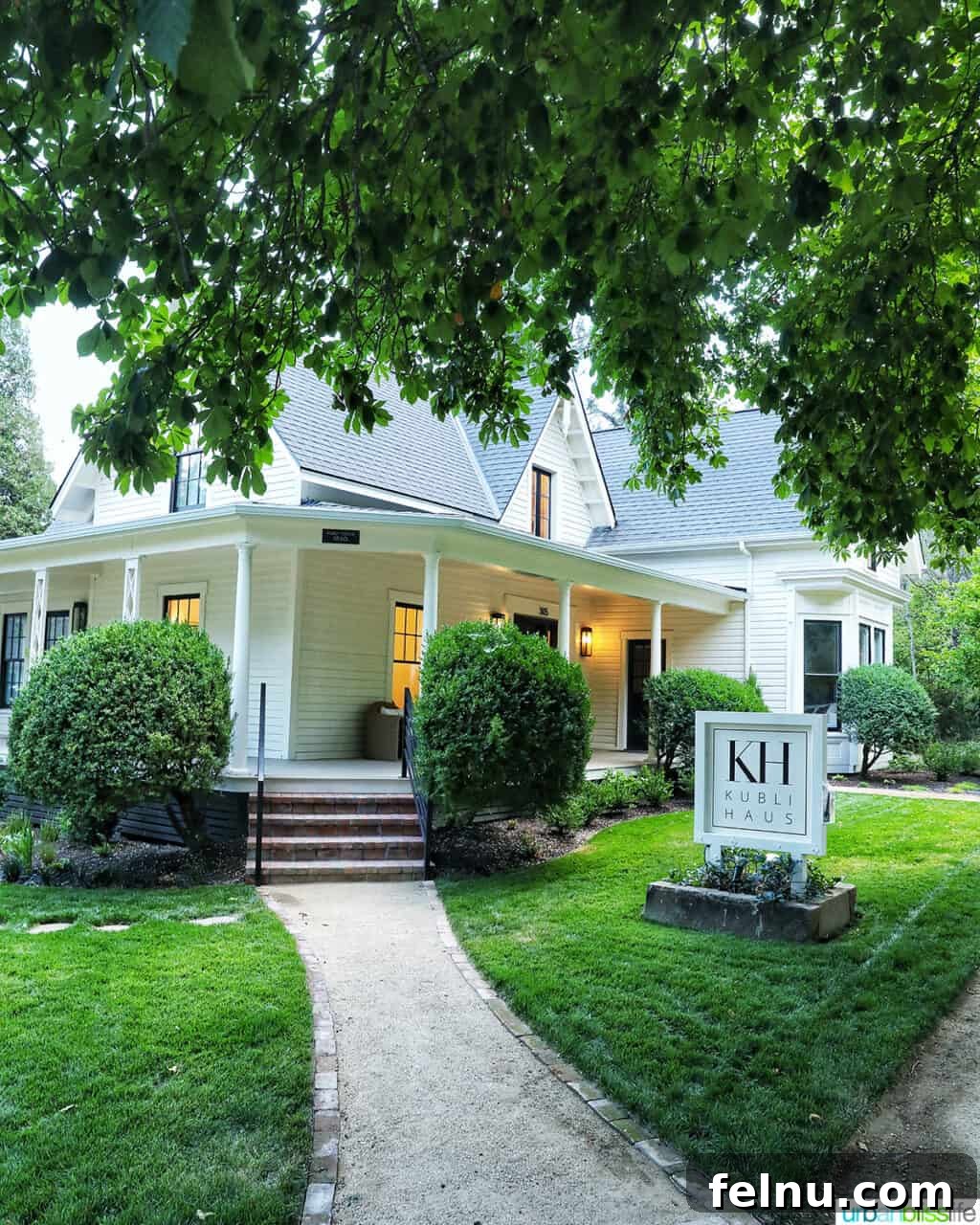The exterior of Kubli Haus hotel in Jacksonville, Oregon, featuring a lush green lawn, welcoming walkway, and graceful overhanging trees.