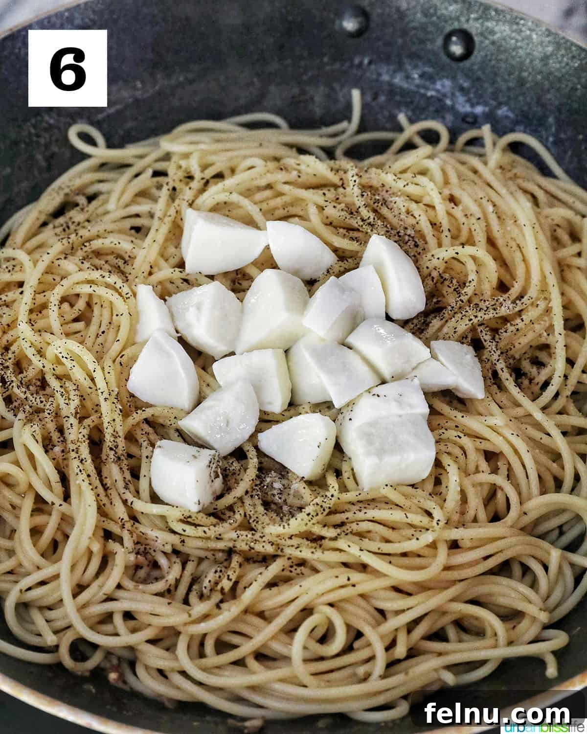 Chopped mozzarella cheese on top of spaghetti in a skillet.