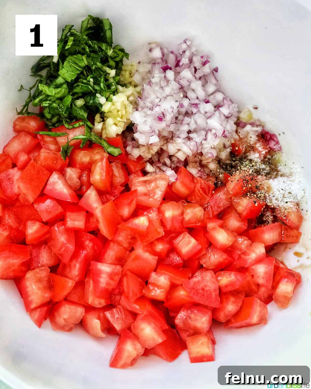 Diced tomatoes, sliced basil, red onions, and garlic in a bowl to make bruschetta.