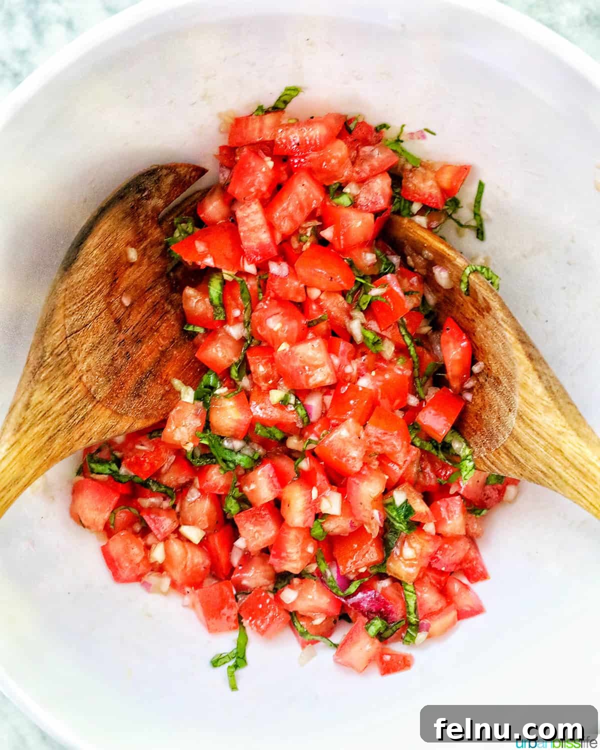 Two wooden spoons tossing bruschetta tomatoes, basil, and garlic.