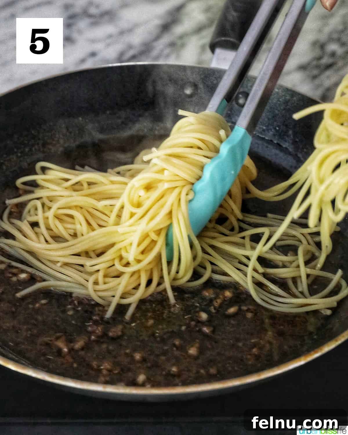 Tongs tossing spaghetti pasta in a skillet.