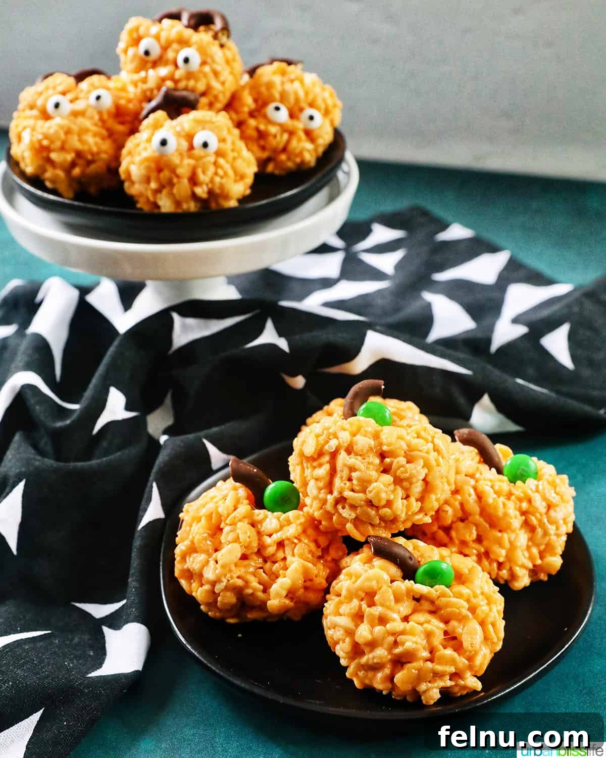 Seasonal Pumpkin Crunch Squares 2 Two decorated orange pumpkin rice krispie treats on black plates with a black and white napkin, showcasing both a silly and a sophisticated style.