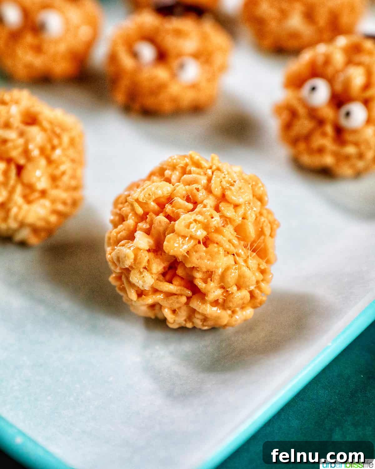 Seasonal Pumpkin Crunch Squares 14 A batch of orange pumpkin rice krispie treats, some decorated and some plain, resting on parchment paper.