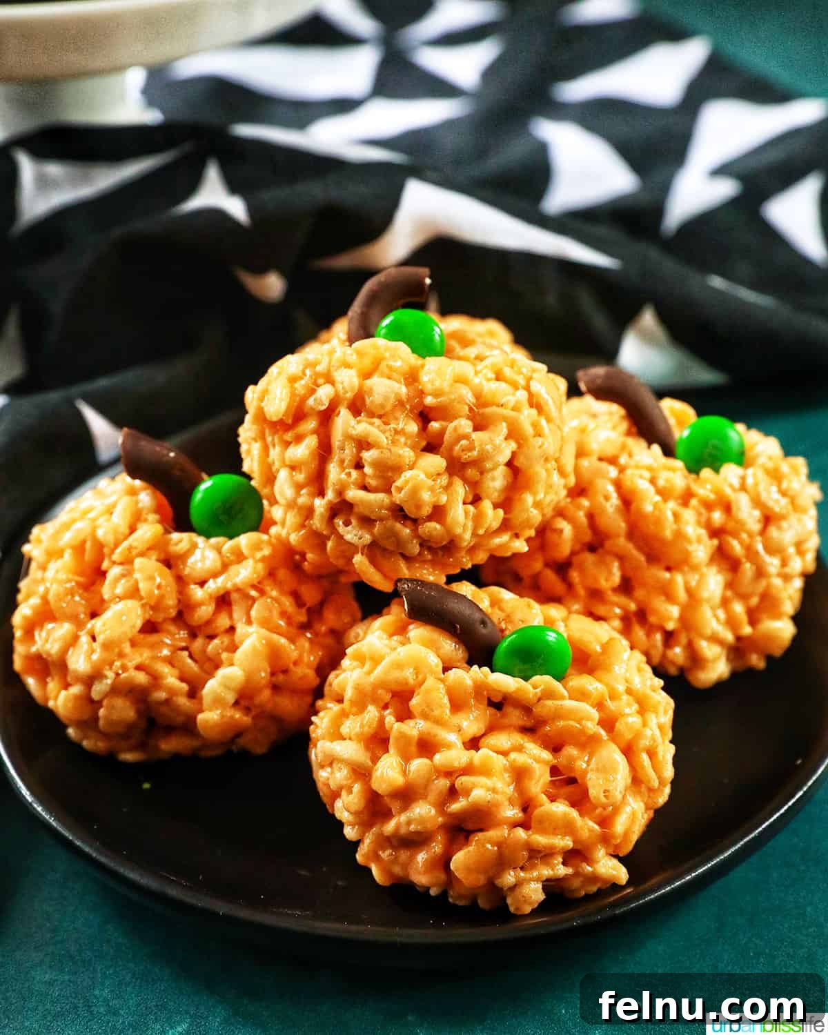 Seasonal Pumpkin Crunch Squares 3 A single orange pumpkin rice krispie treat adorned with a pretzel stem and a green candy leaf, placed on a black plate.