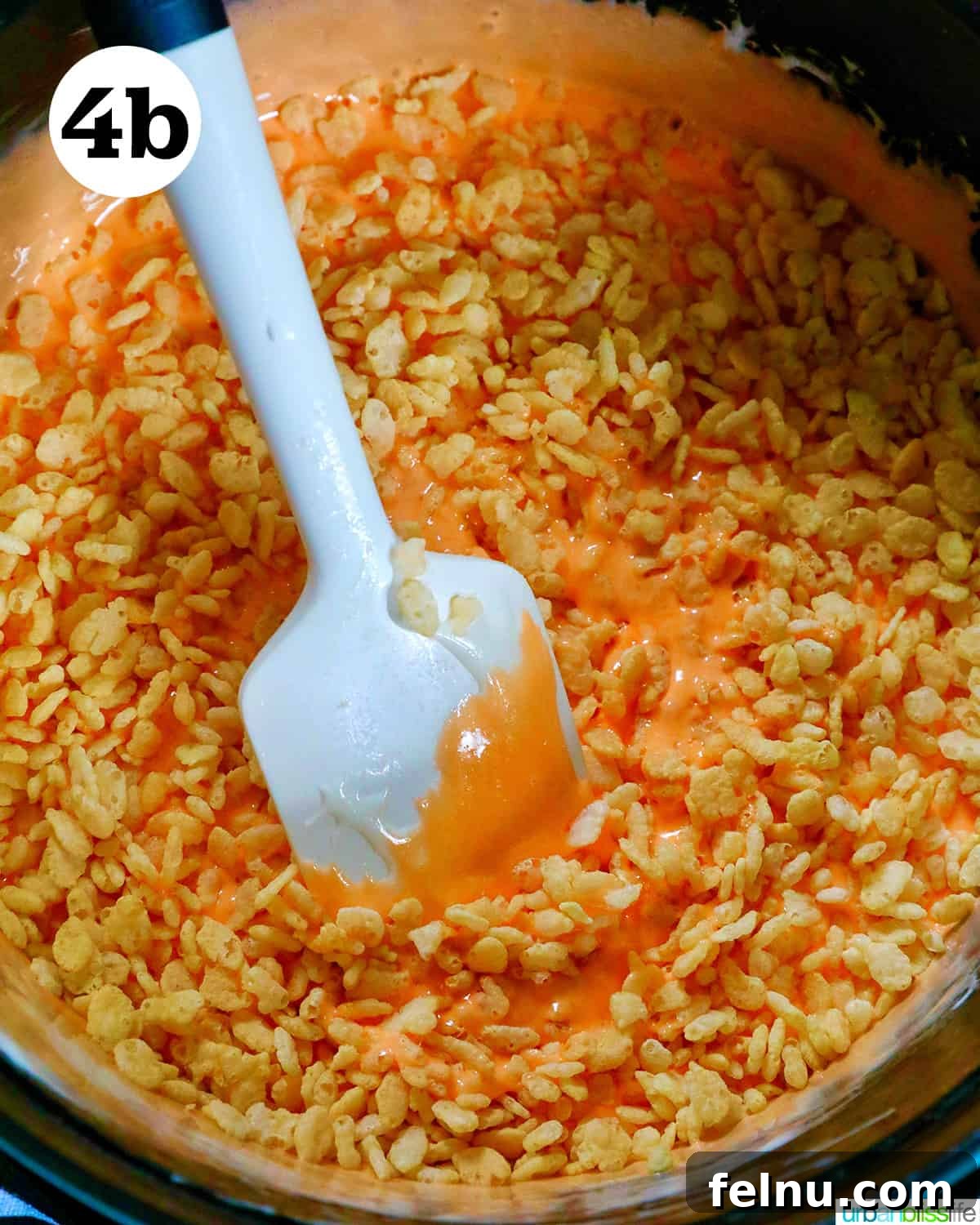 Seasonal Pumpkin Crunch Squares 10 A spatula gently stirring Rice Krispies cereal into the orange marshmallow mixture.