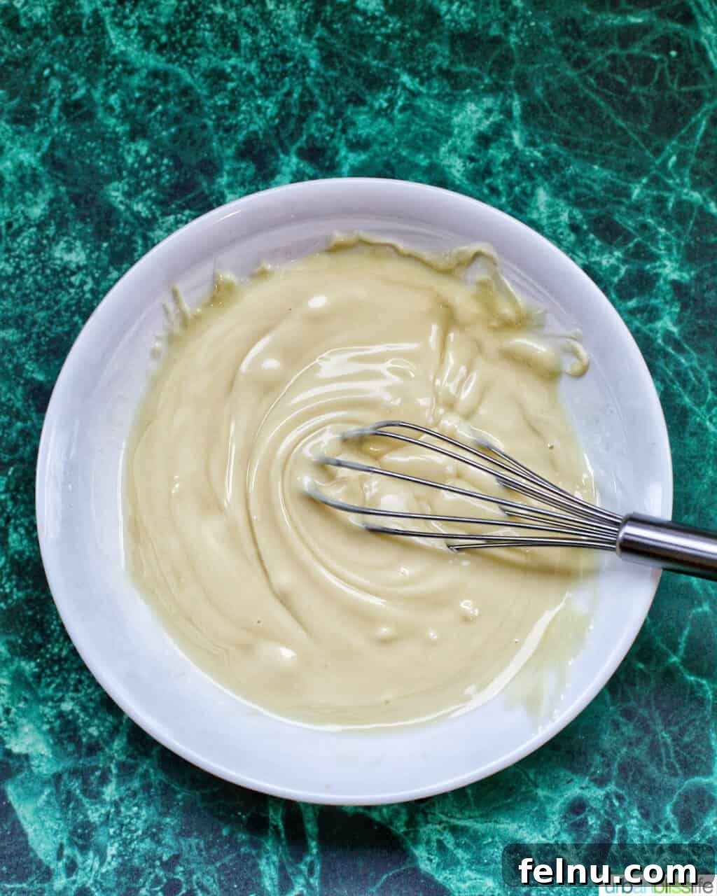 Festive Holiday Popcorn Mix 7 melted white chocolate in a bowl with a small whisk