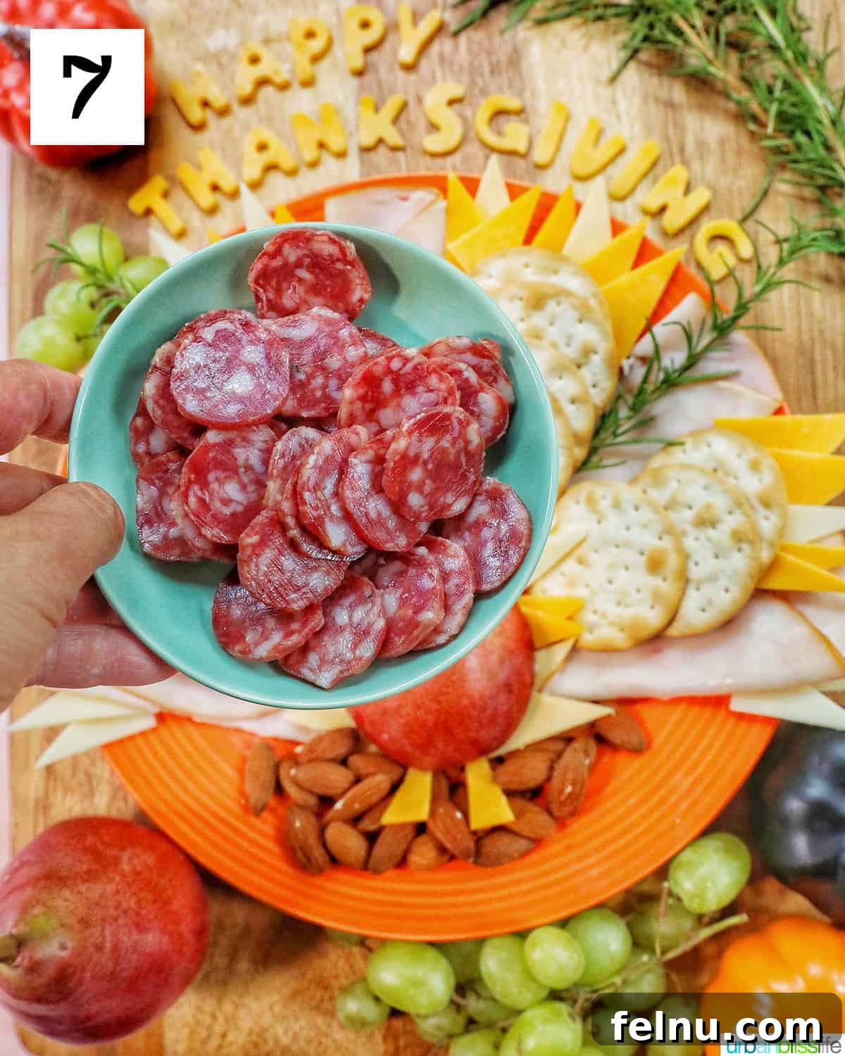 hand holding a plate of sliced salami over a Thanksgiving charcuterie board.