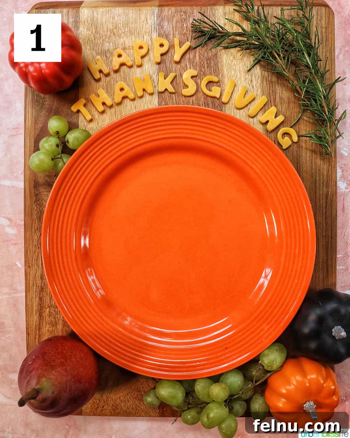 First layer of a Thanksgiving charcuterie board with Happy Thanksgiving cheese, orange plate, fruit on a wood board.