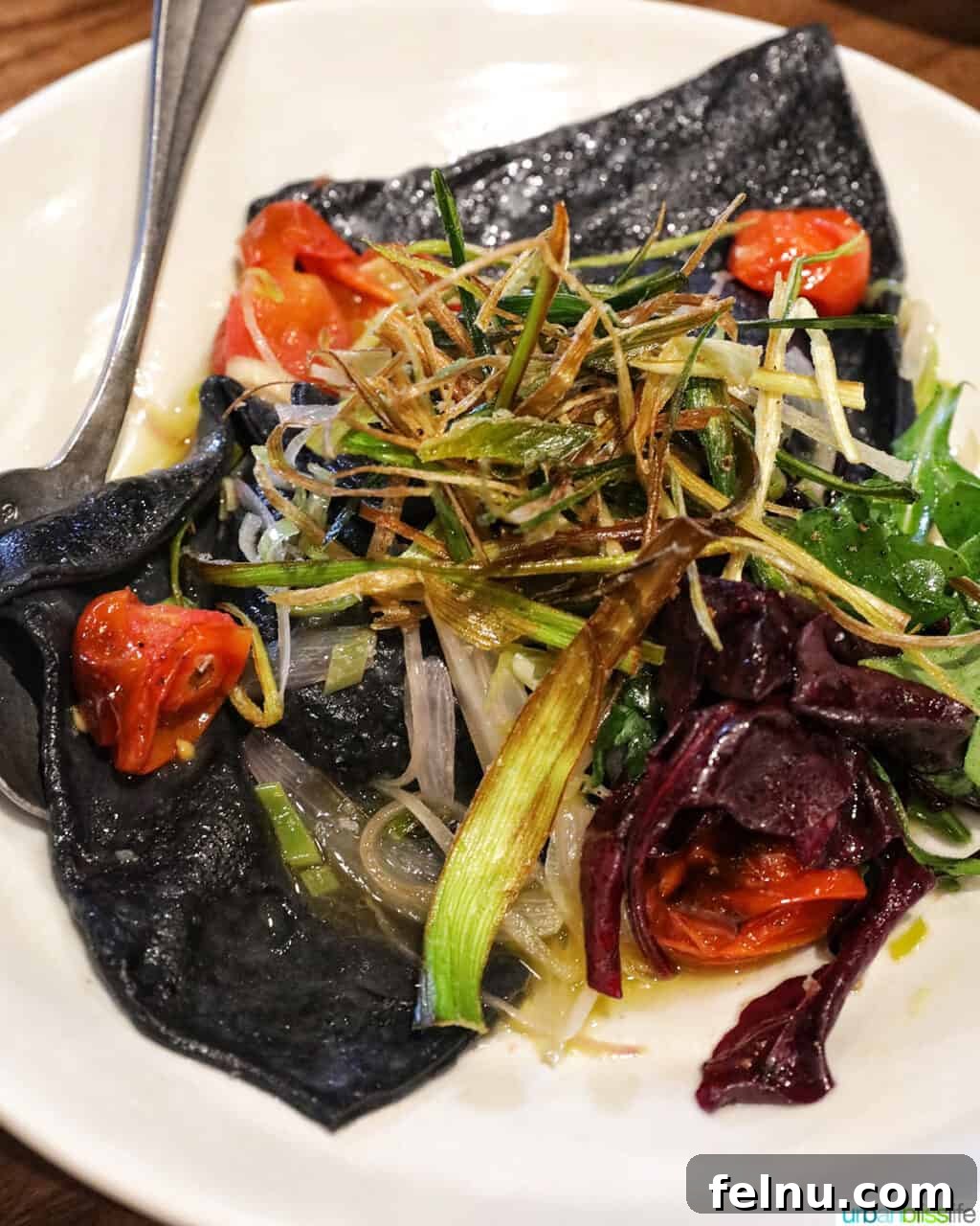 Banff Unleashed 12 Mushroom ravioli with blistered tomatoes and leeks on a white plate, showcasing its dark charcoal pasta.