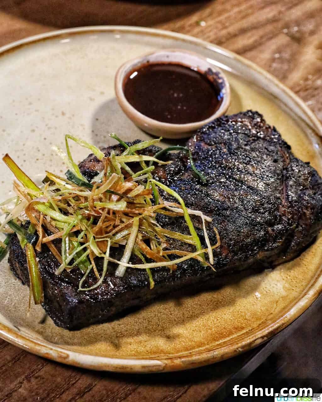 Banff Unleashed 13 Coffee rubbed steak topped with crispy leeks and a side of jus on a plate, a hearty mountain meal.