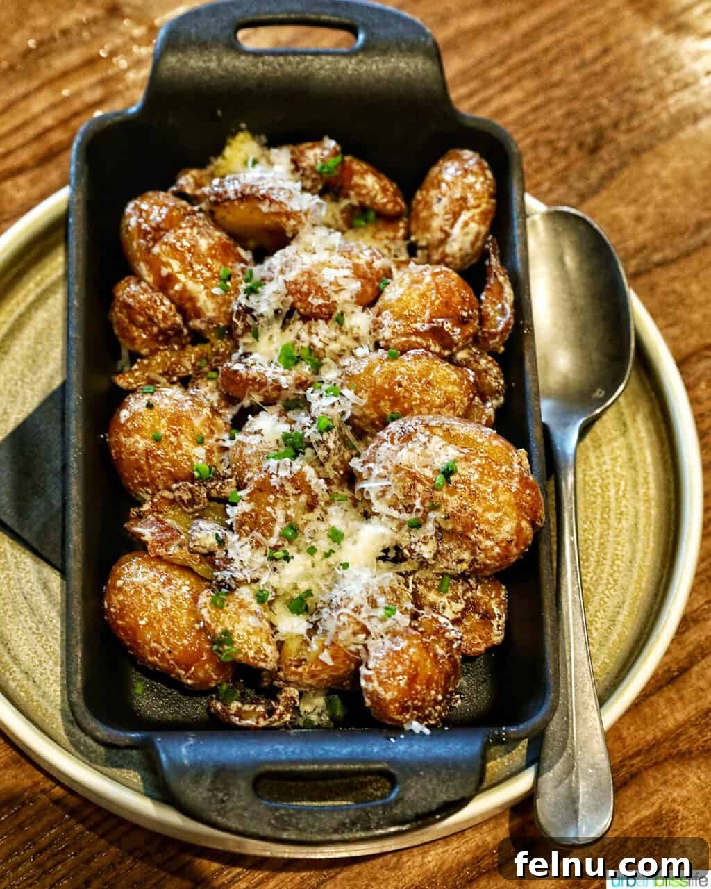 Banff Unleashed 6 Parmesan truffle potatoes in a cast iron serving plate with a spoon, rich and golden.