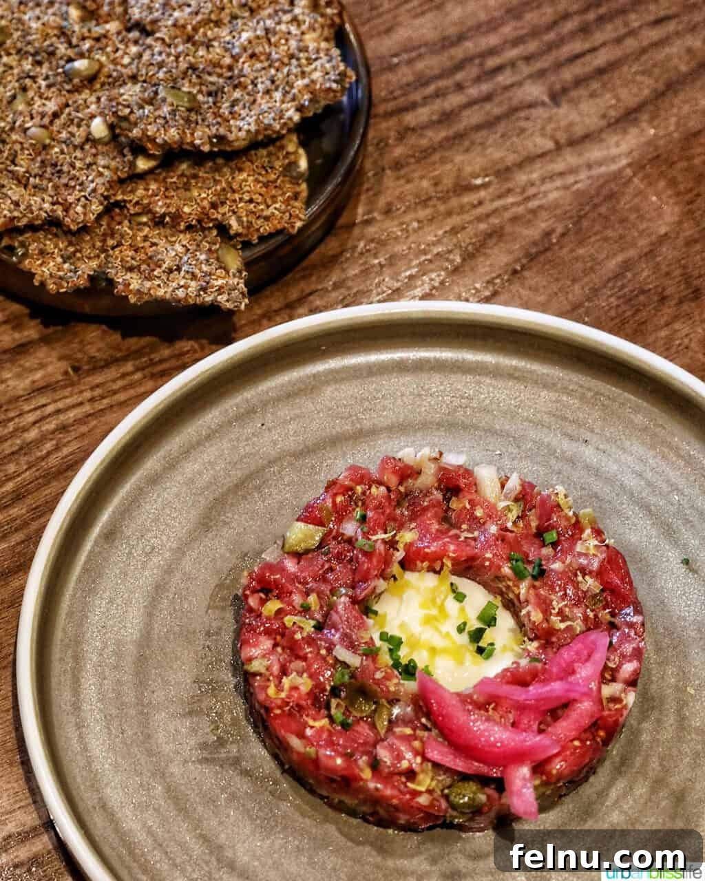 Banff Unleashed 7 Bison tartare on a cream-colored plate with a side of quinoa crackers, elegantly presented.