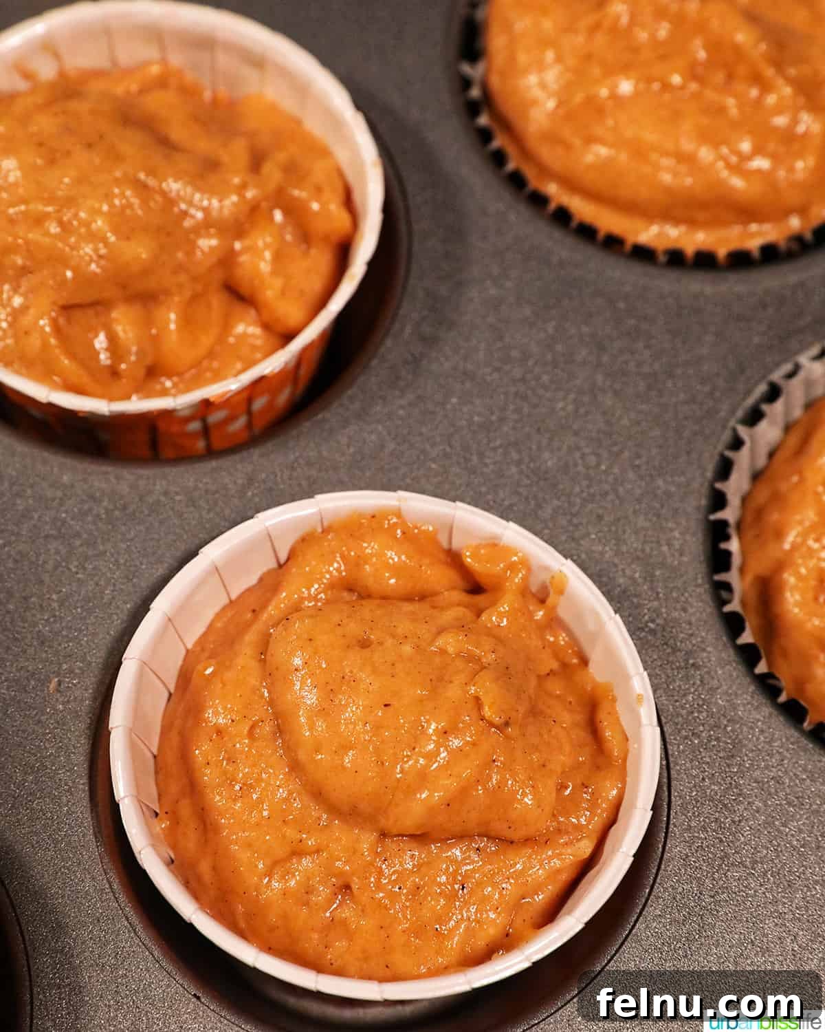 Pumpkin Banana Bliss Muffins 12 Muffin cups filled with orange pumpkin banana muffin batter in a muffin tin.