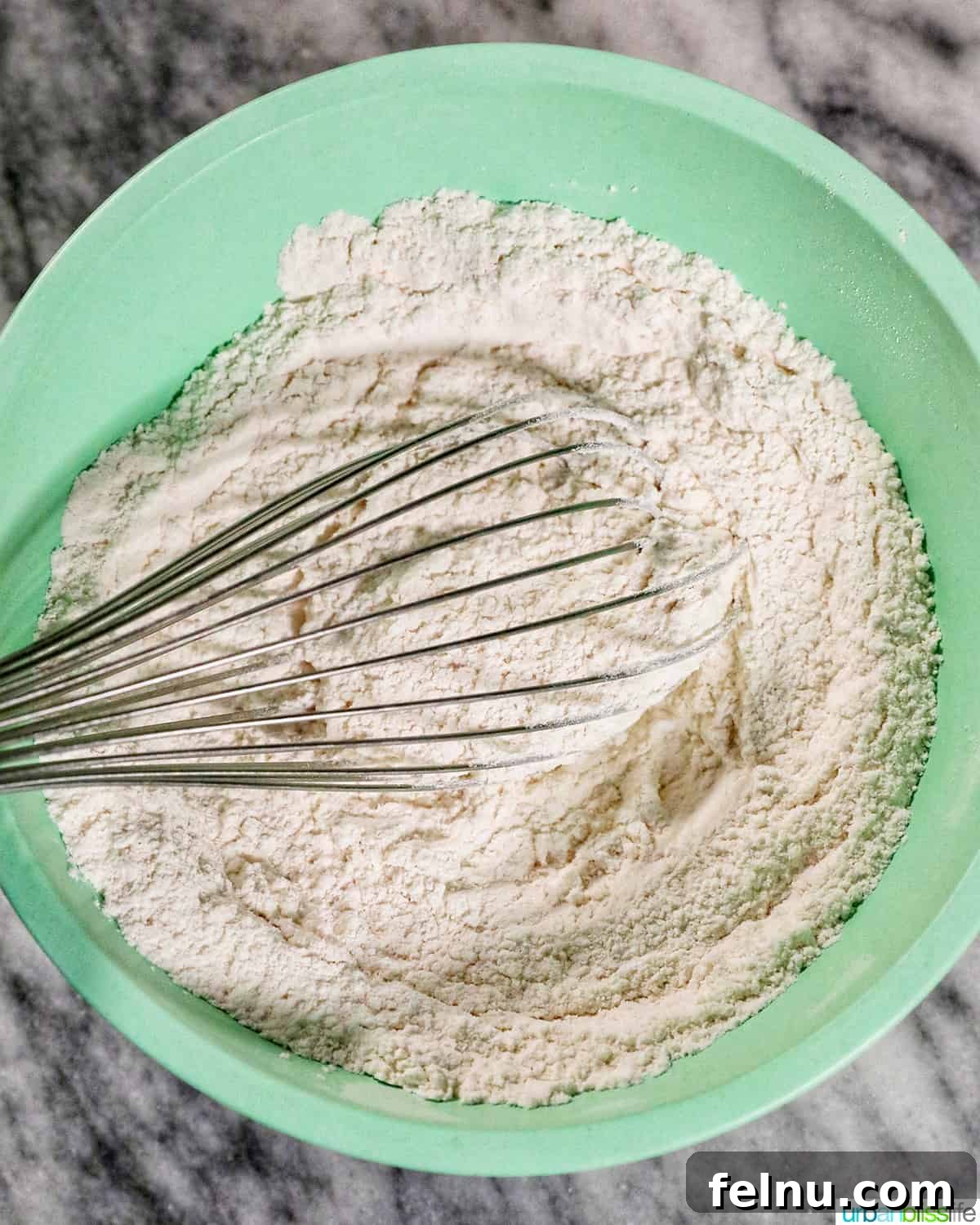 Fluffy Air Fryer Biscuits 5 whisk with dry baking ingredients in a green bowl.