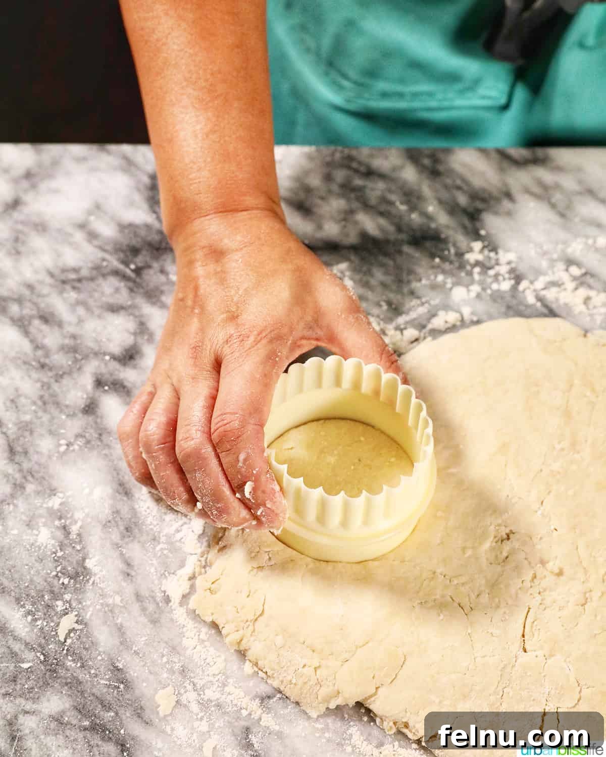 Fluffy Air Fryer Biscuits 10 hand holding a biscuit cutter over biscuit dough on a marble counter.