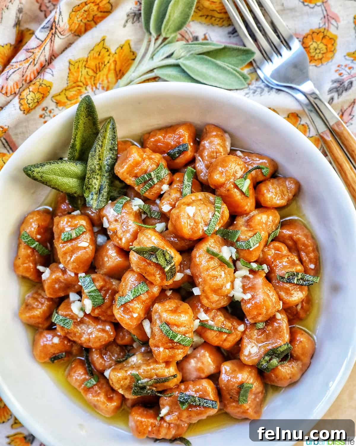 A beautifully presented bowl of homemade pumpkin gnocchi, garnished with fresh sage, next to a fork and a colorful napkin, inviting diners to savor the autumn flavors.