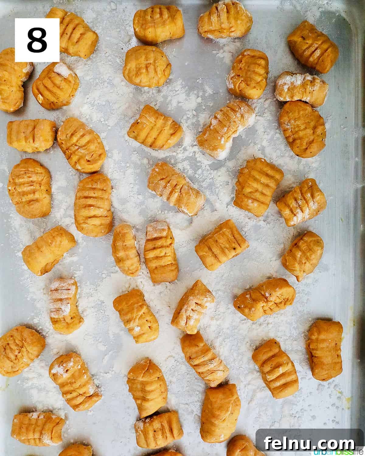 Neatly shaped pumpkin gnocchi pieces, each with characteristic ridges, rest on a sheet of parchment paper, ready for cooking.
