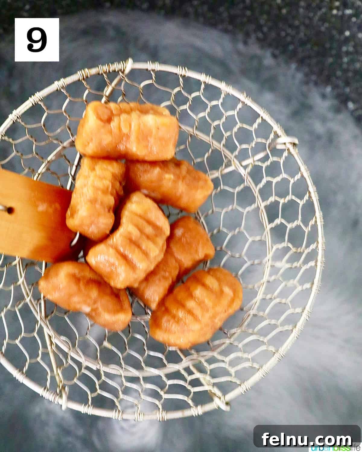 A wire kitchen spider carefully lifts freshly cooked, shaped pumpkin gnocchi out of boiling water, ensuring each piece is perfectly al dente before being transferred.
