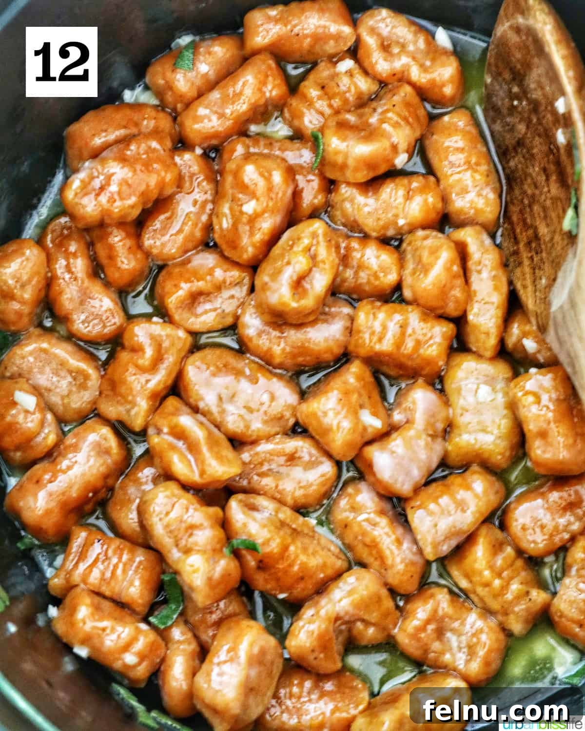 Freshly shaped pumpkin gnocchi pieces are gently tossed and coated in a rich, simmering sage butter sauce within a pan, infusing them with savory flavors.