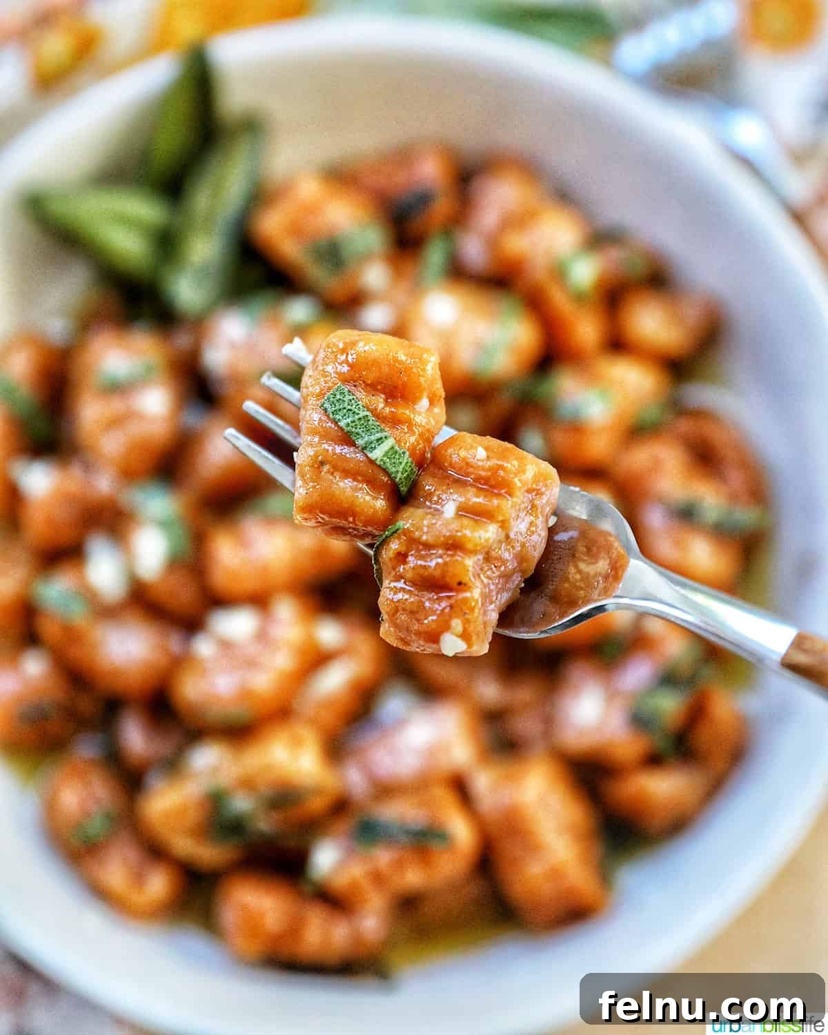 A fork lifts two pieces of pumpkin gnocchi, captured in a delicious close-up, hovering just above a full bowl of the gnocchi dish, emphasizing its appetizing texture and presentation.