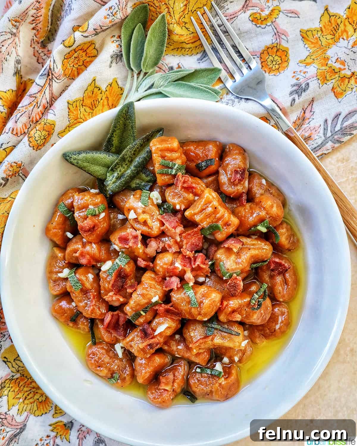 A full bowl of autumnal pumpkin gnocchi with crispy bacon and fresh sage leaves, ready to be enjoyed, with a fork and colorful napkin nearby.