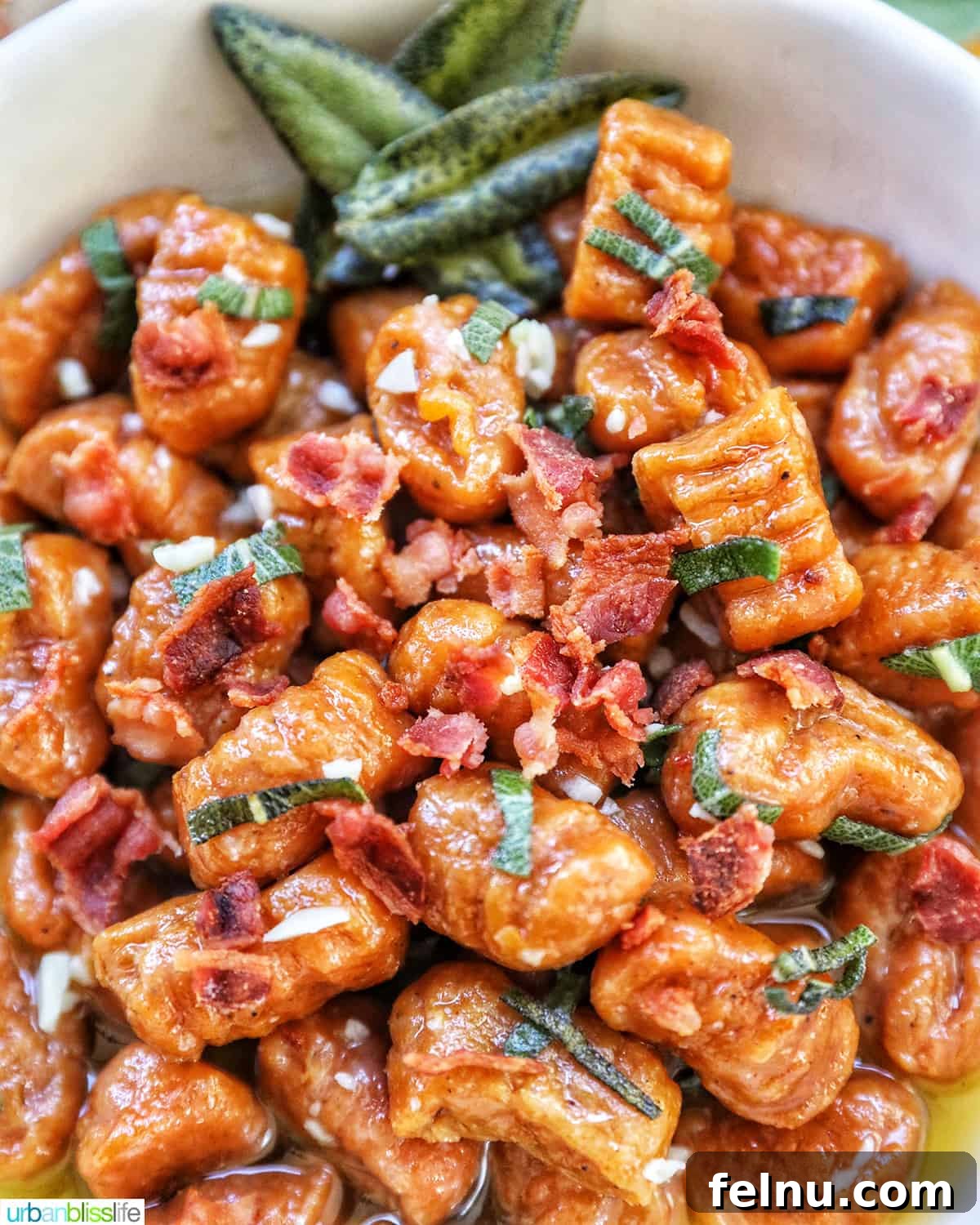 A close-up view of homemade pumpkin gnocchi generously coated in sage butter sauce, featuring crispy bacon bits and fresh sage leaves as garnish, highlighting its rich textures and autumnal appeal.