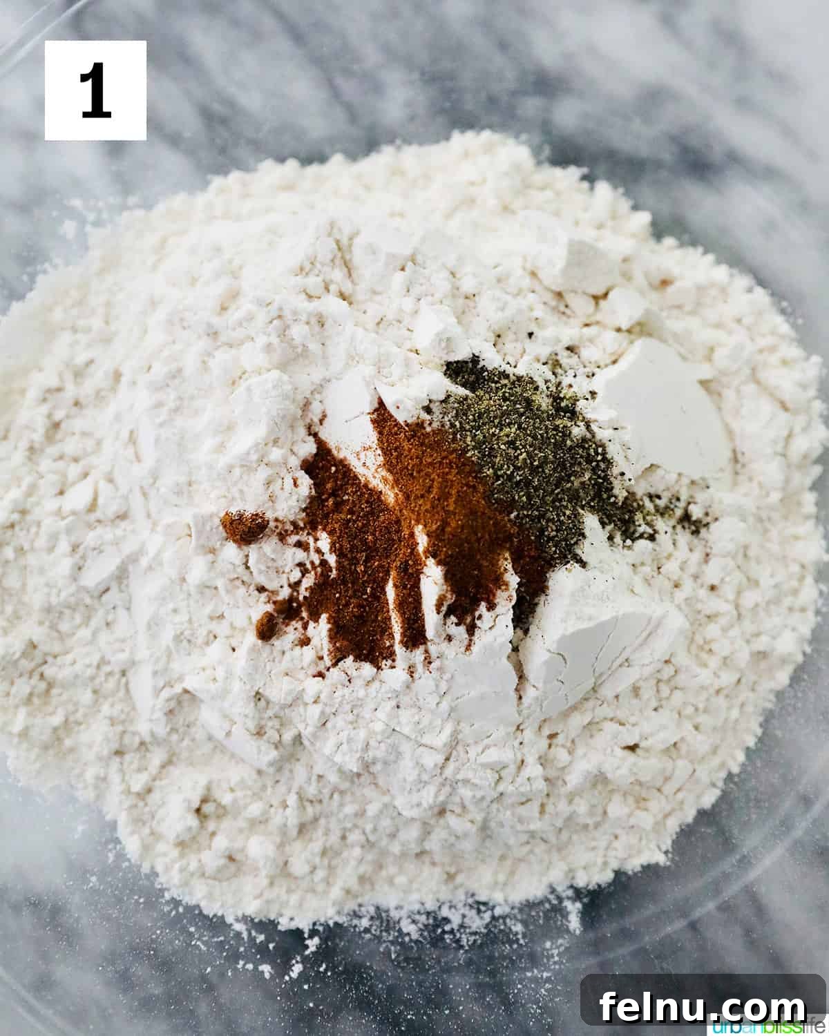 A bowl on a marble countertop containing dry ingredients like flour, salt, pepper, and nutmeg, all whisked together and ready for the next step in preparing pumpkin gnocchi.