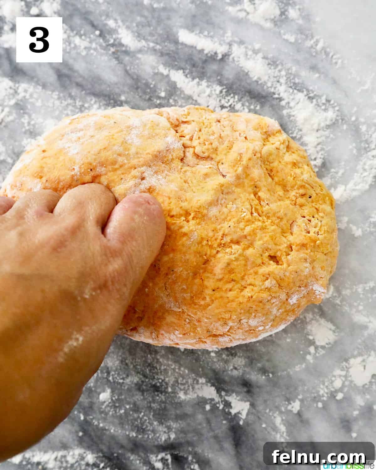 Hands are shown gently kneading pumpkin gnocchi dough on a lightly floured marble countertop, illustrating the process of forming a soft, cohesive dough.