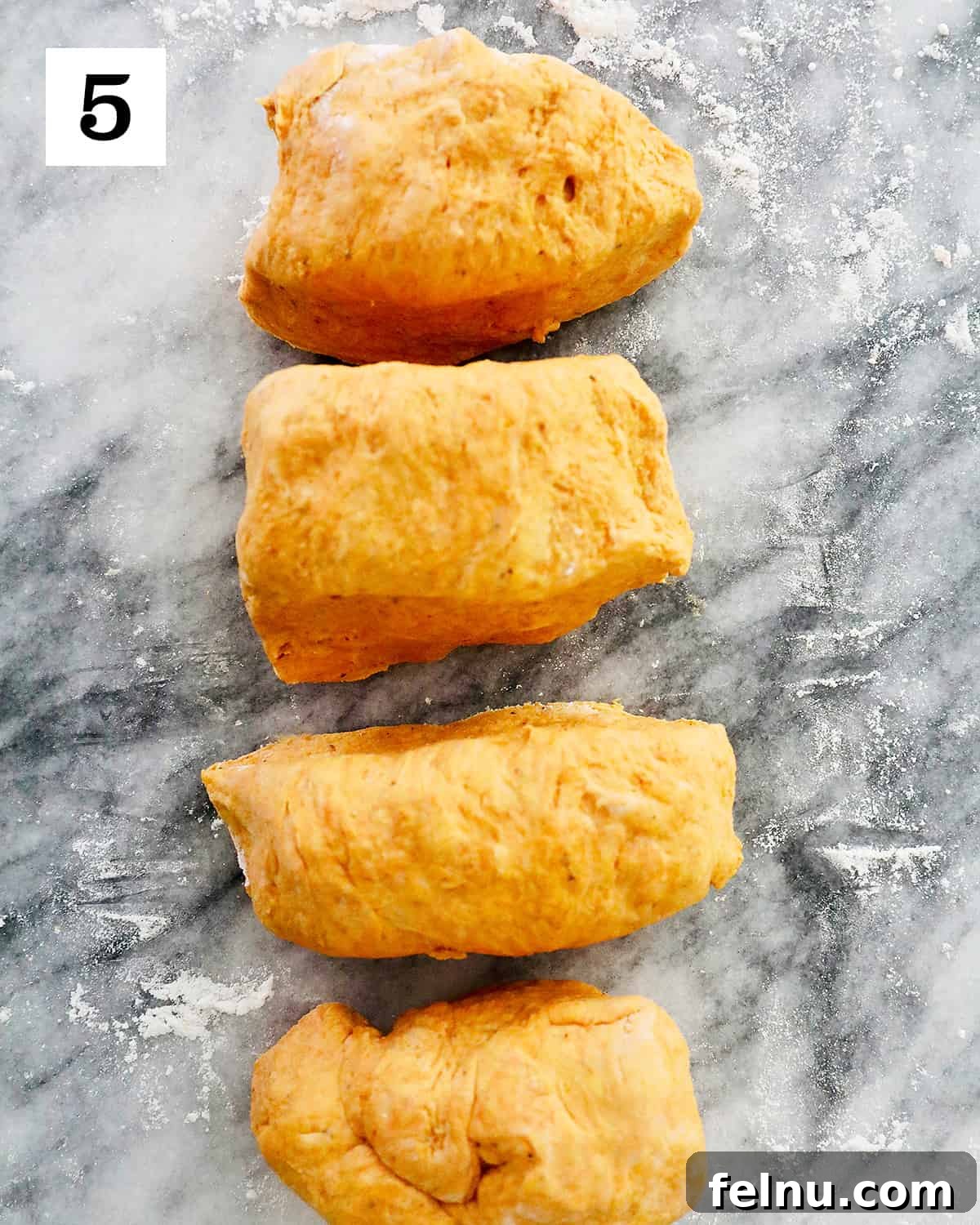 A ball of pumpkin gnocchi dough is neatly divided into four equal portions on a marble countertop, preparing for the rolling and shaping stages.