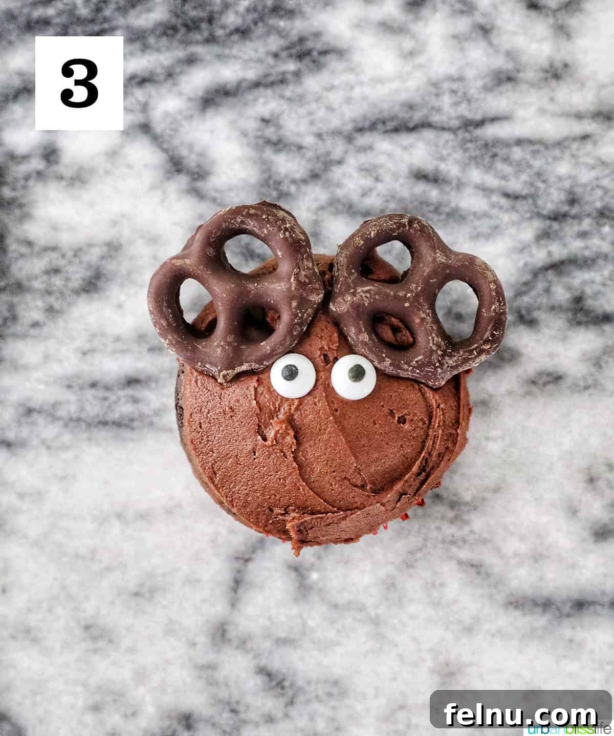 Reindeer Delight Cupcakes 15 Adding candy eyes to a chocolate frosted cupcake with pretzel ears