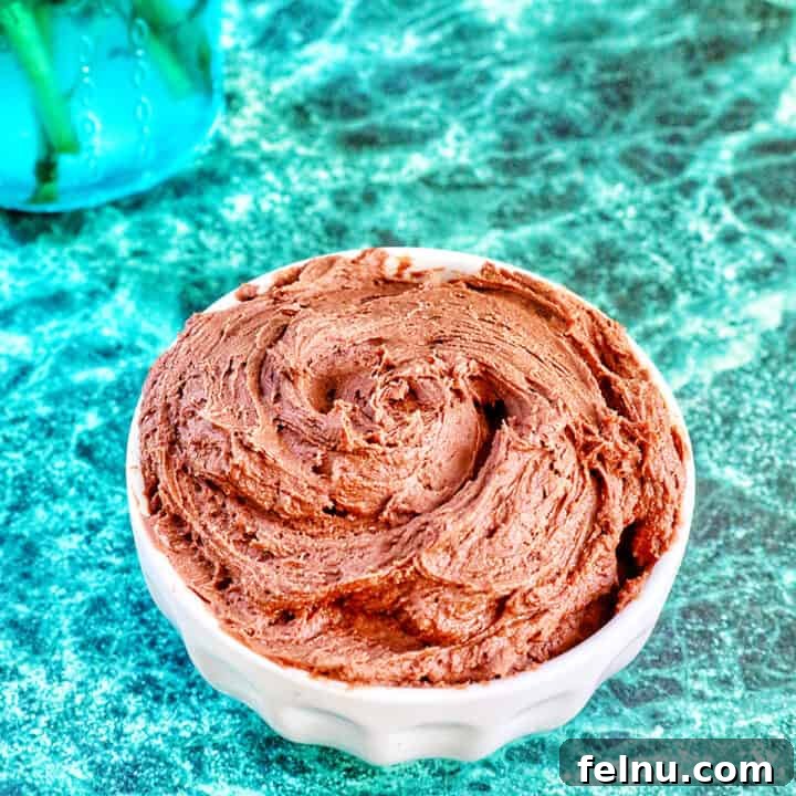chocolate buttercream frosting in a white bowl on a green marble table.