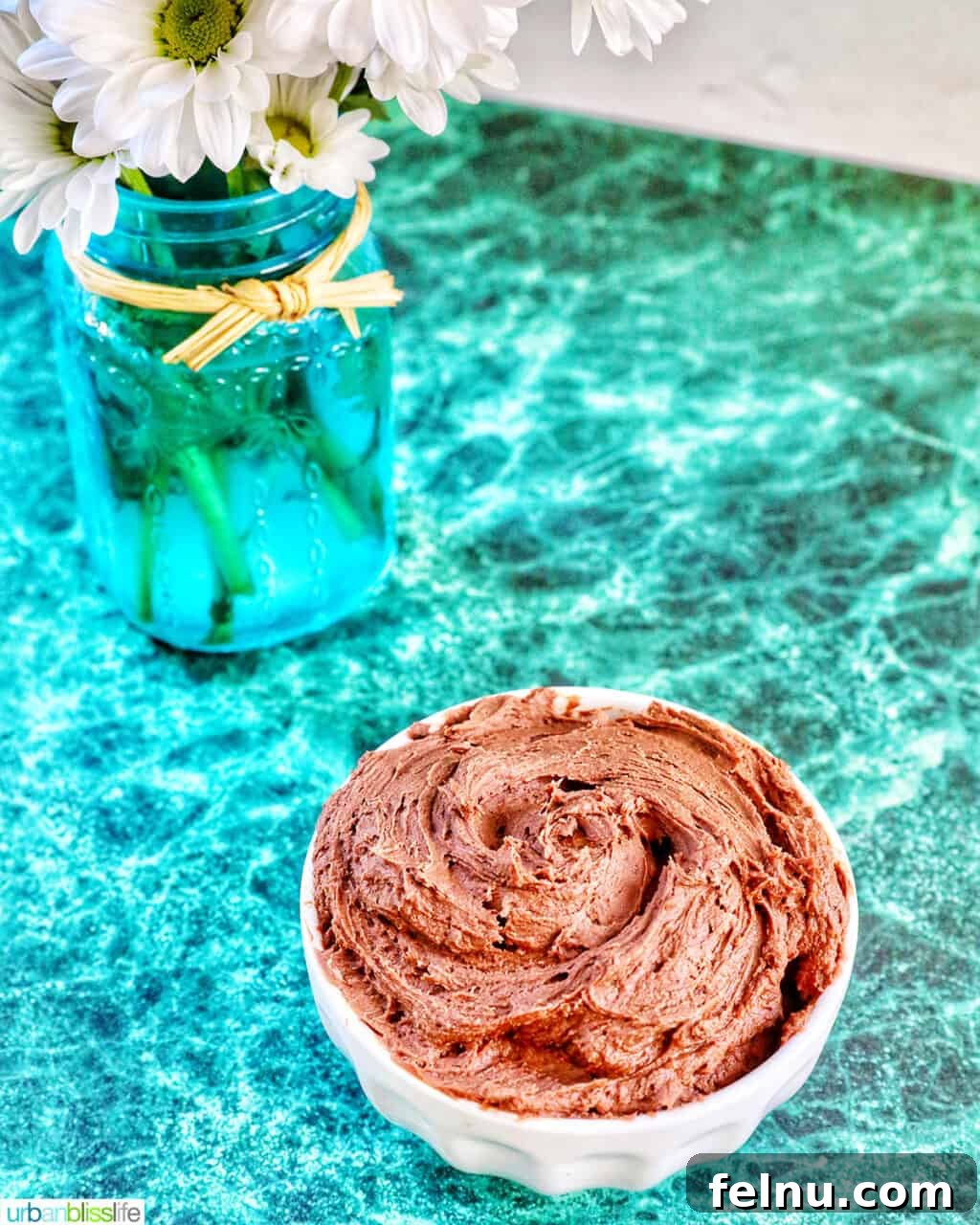 Effortless Decadent Chocolate Buttercream 3 A close-up shot of decadent chocolate buttercream frosting in a white bowl, resting on a green marble countertop, highlighting its smooth texture.