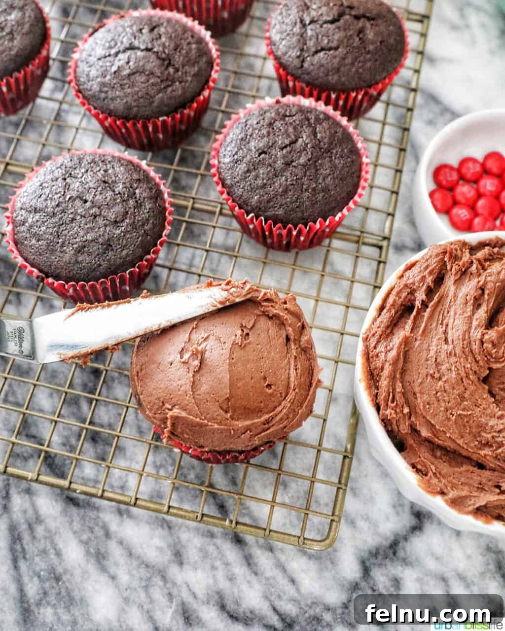 Effortless Decadent Chocolate Buttercream 8 A hand frosting a rich chocolate cupcake with a generous swirl of chocolate buttercream, with more cupcakes blurred in the background.