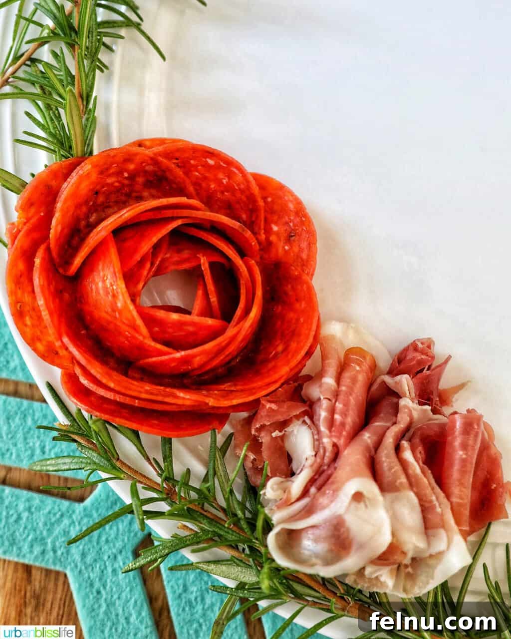 A Festive Christmas Snack Board 8 A close-up of prosciutto paired with a pepperoni rose and sprigs of fresh rosemary on a Christmas charcuterie board.