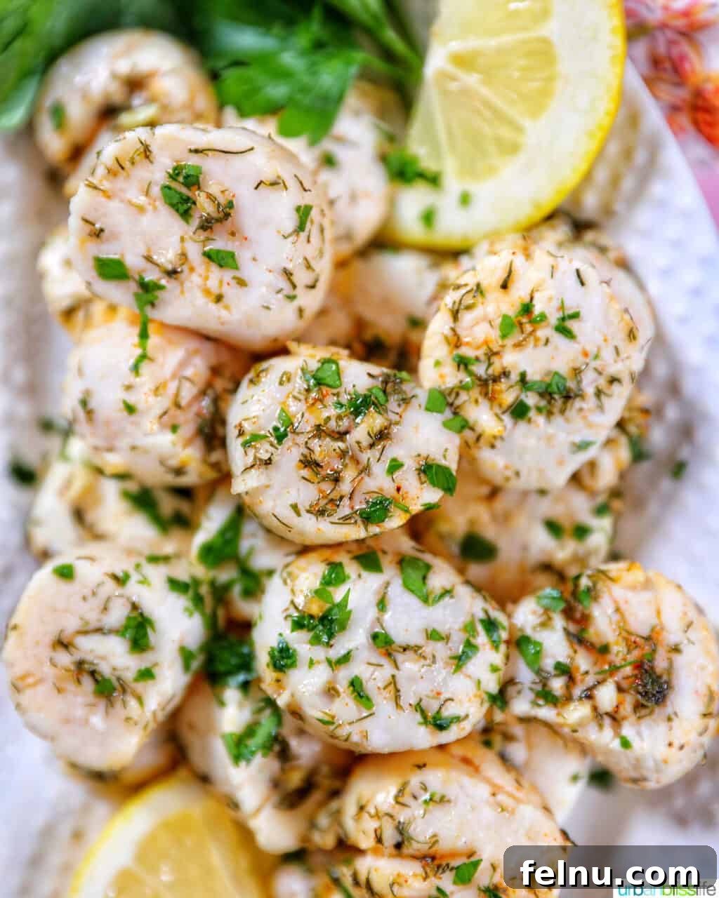 Golden Air Fryer Scallops 2 several cooked scallops topped with herbs and garlic, with lemon slices and parsley, on a white plate.