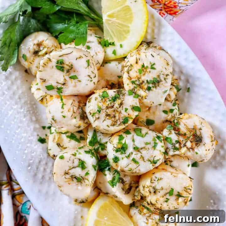 Golden Air Fryer Scallops 10 several cooked scallops topped with herbs and garlic, with lemon slices and parsley, on a white plate.