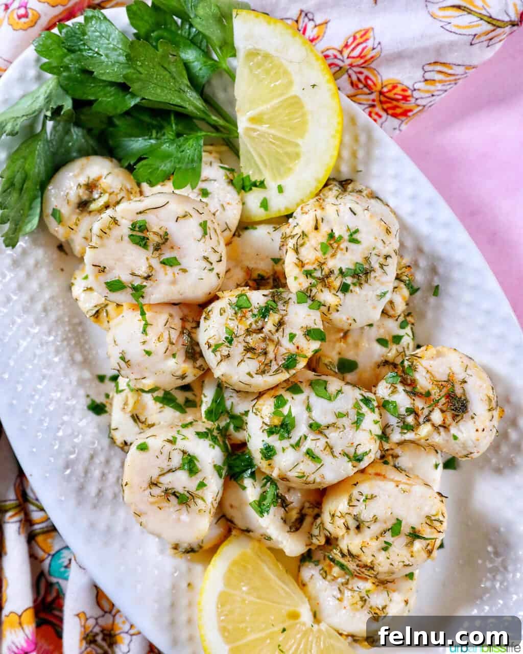 Golden Air Fryer Scallops 3 several cooked scallops topped with herbs and garlic, with lemon slices and parsley, on a white plate.