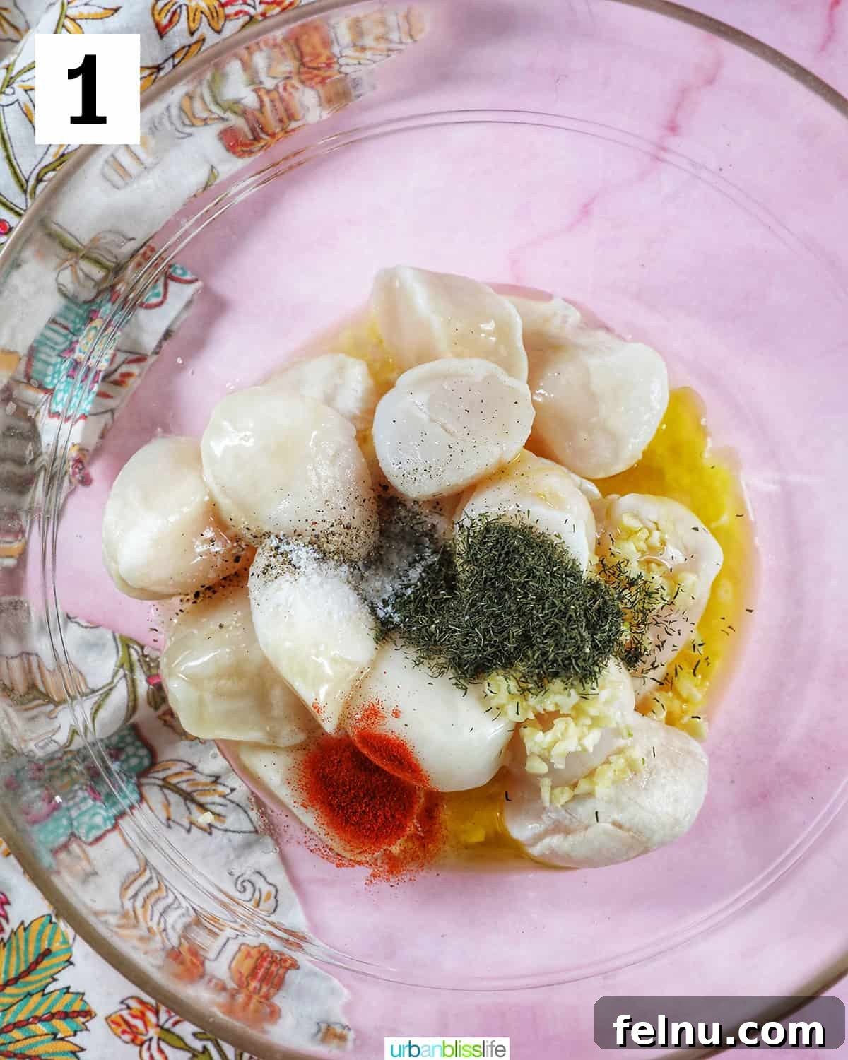 Golden Air Fryer Scallops 5 scallops, garlic, herbs, spices in a clear glass bowl on pink table.